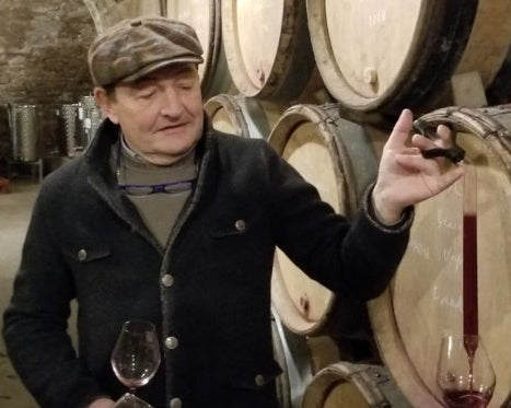 Man tasting wine in a cellar with barrels and another person holding a glass.