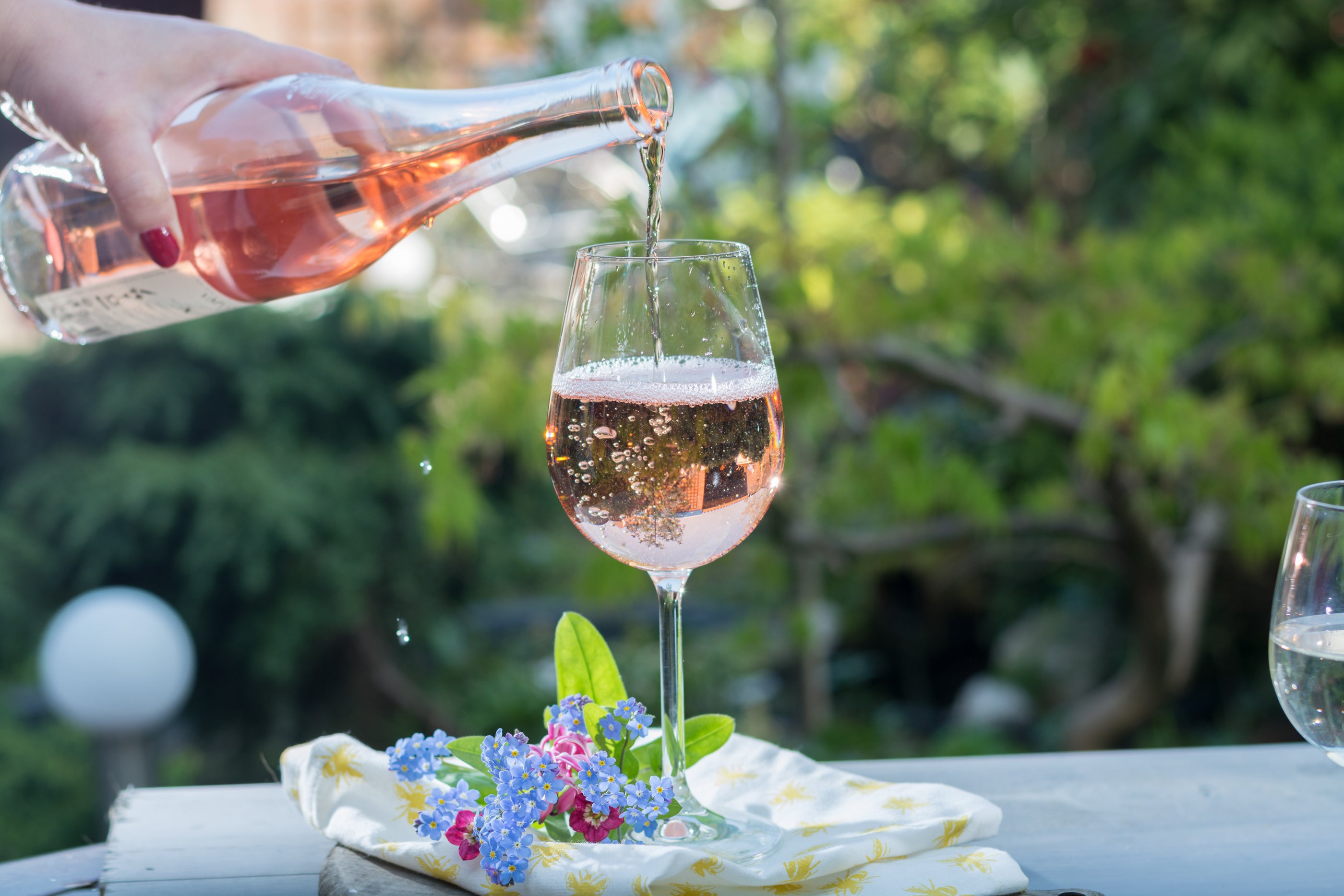 Rose wine being poured into a glass with a blurred garden background
