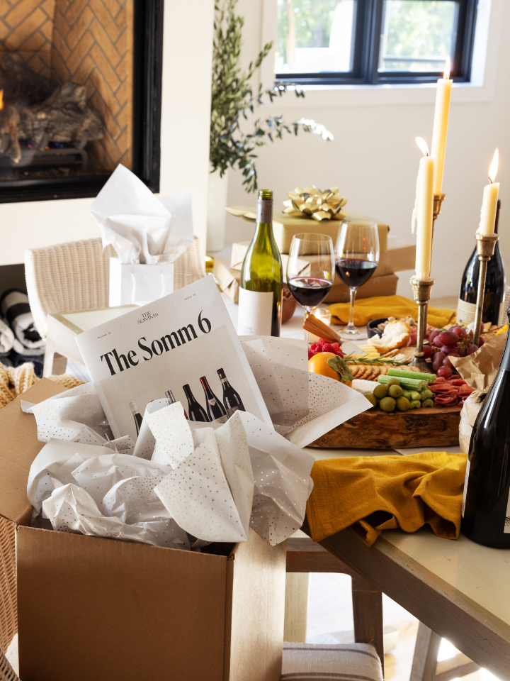 Table setting with wine bottles, glasses, and a magazine titled 'The Somm 6' in a cozy room.