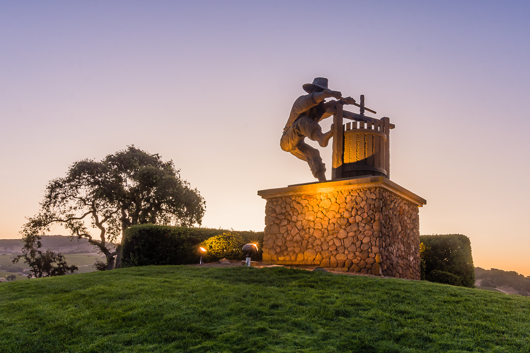 Person sitting on a stone bench with a view of a scenic landscape at sunset.